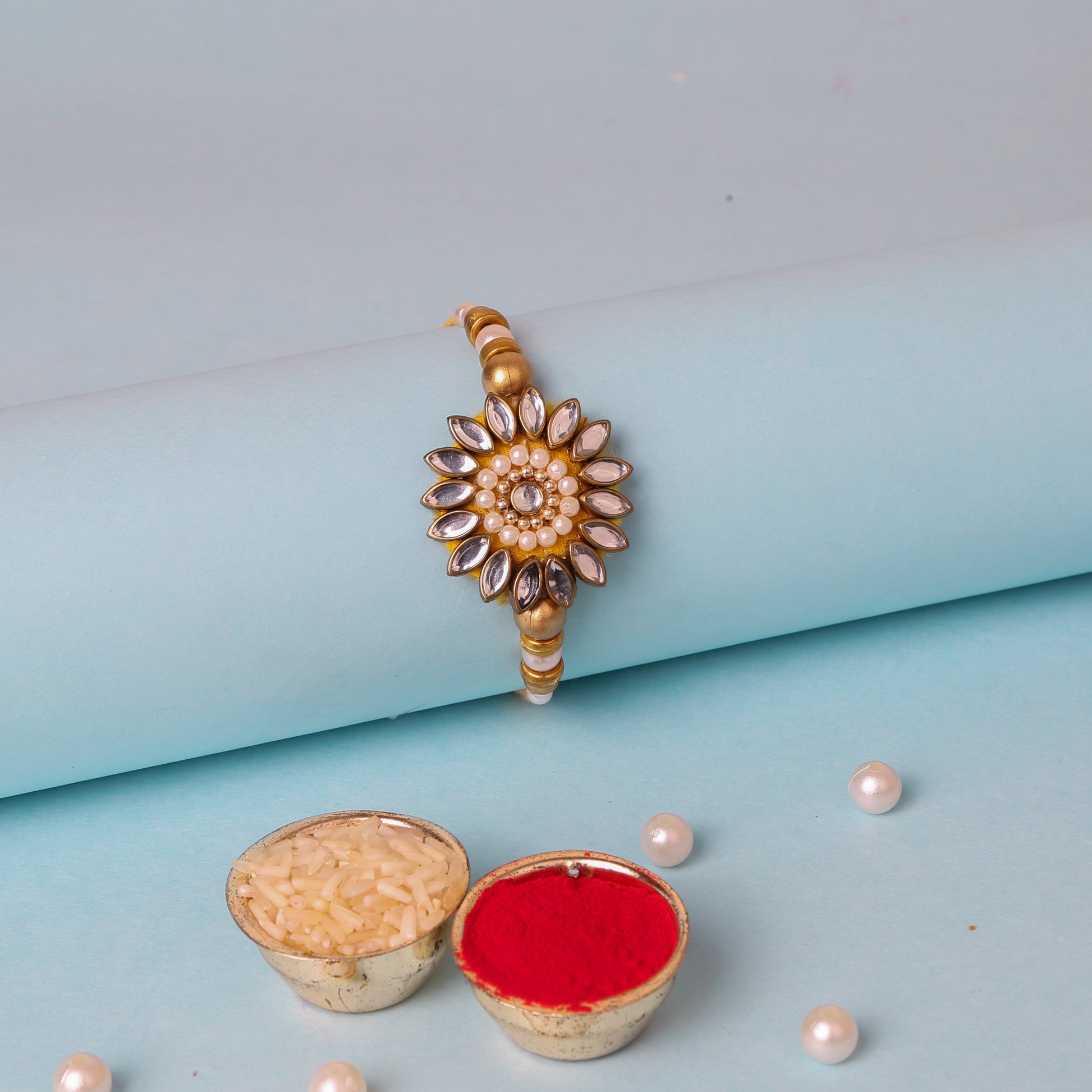 A gold and white rakhi with a flower, adorned with kundan stones and beautiful beads.