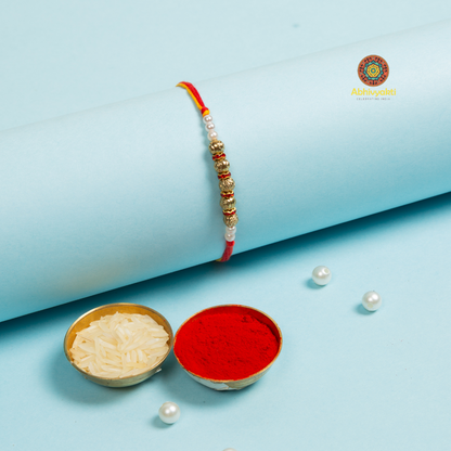 A lovely rakhi featuring red and gold beads, along with a pearl.