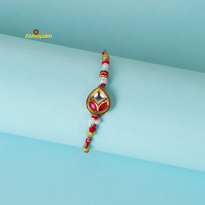 Kundan rakhi with red and green colors, adorned with gold and green stone and lovely beads