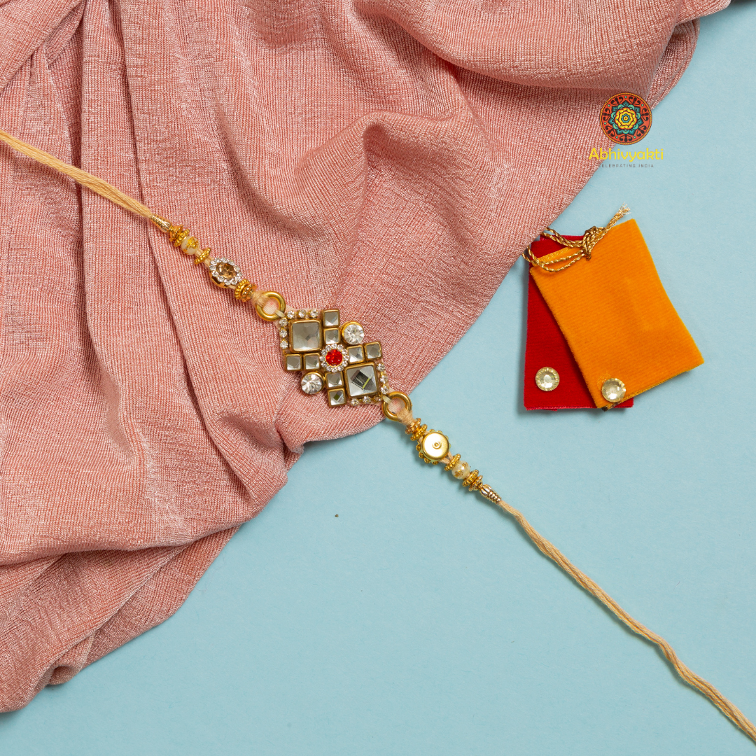 Gold and orange rakhi with red and orange cloth, embellished with stones and beads.