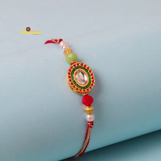 Kundan rakhi with red and green colors, adorned with gold and green stone and lovely beads.