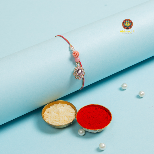 Elegant pink rakhi adorned with pearls and a single pearl, featuring stone and bead details.