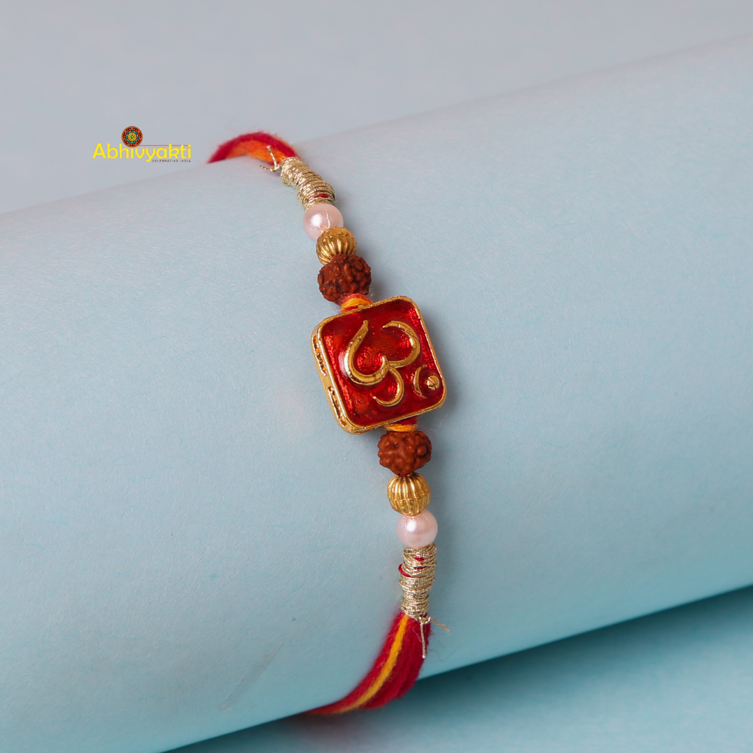 An om rakhi with beads, showcasing a red and yellow thread band adorned with golden and rudraksha beads, features a red square centerpiece with a gold "Om" symbol, displayed against a pastel blue background.