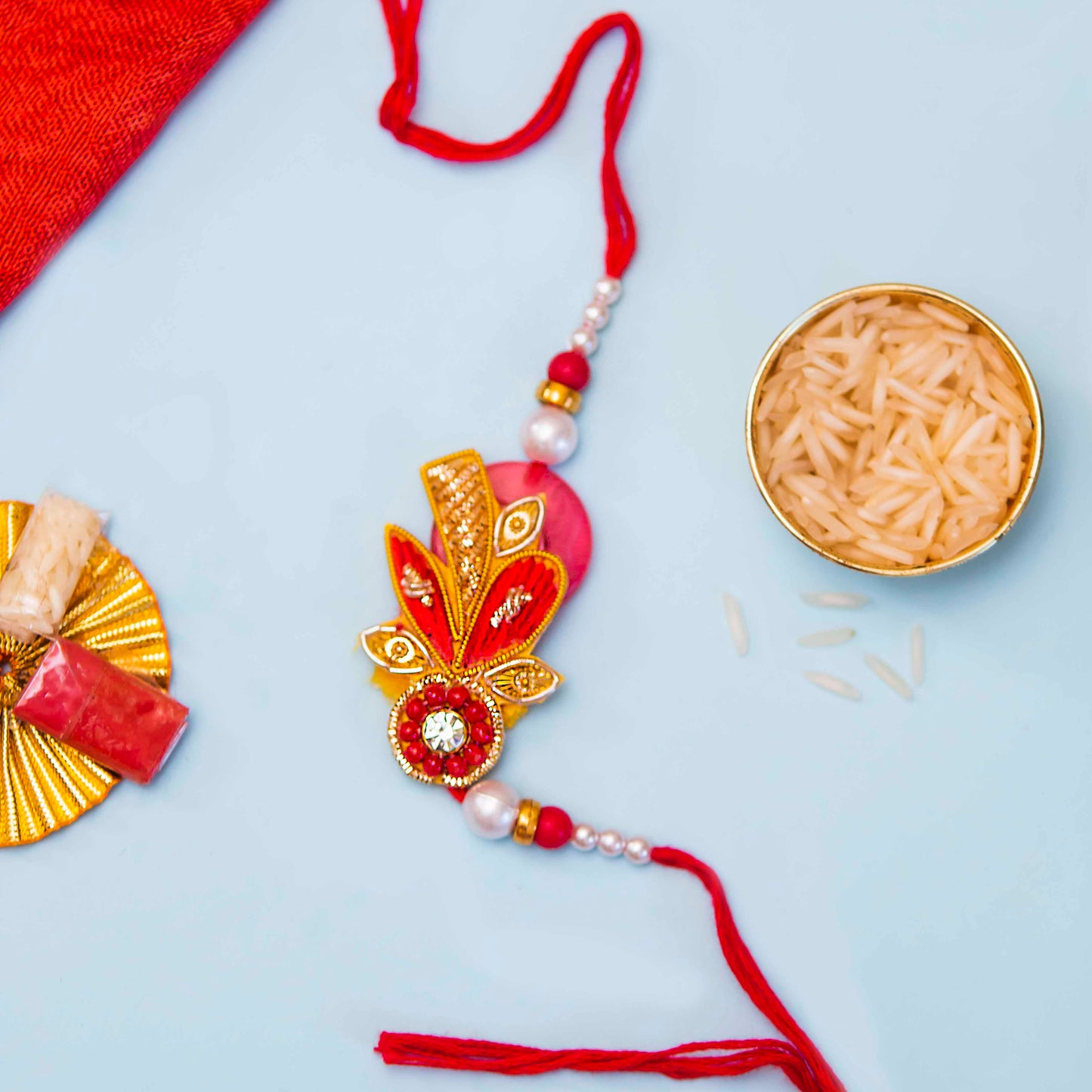 Elegant red and gold rakhi adorned with a gold bead, showcasing a unique zari design with lovely beads and stone