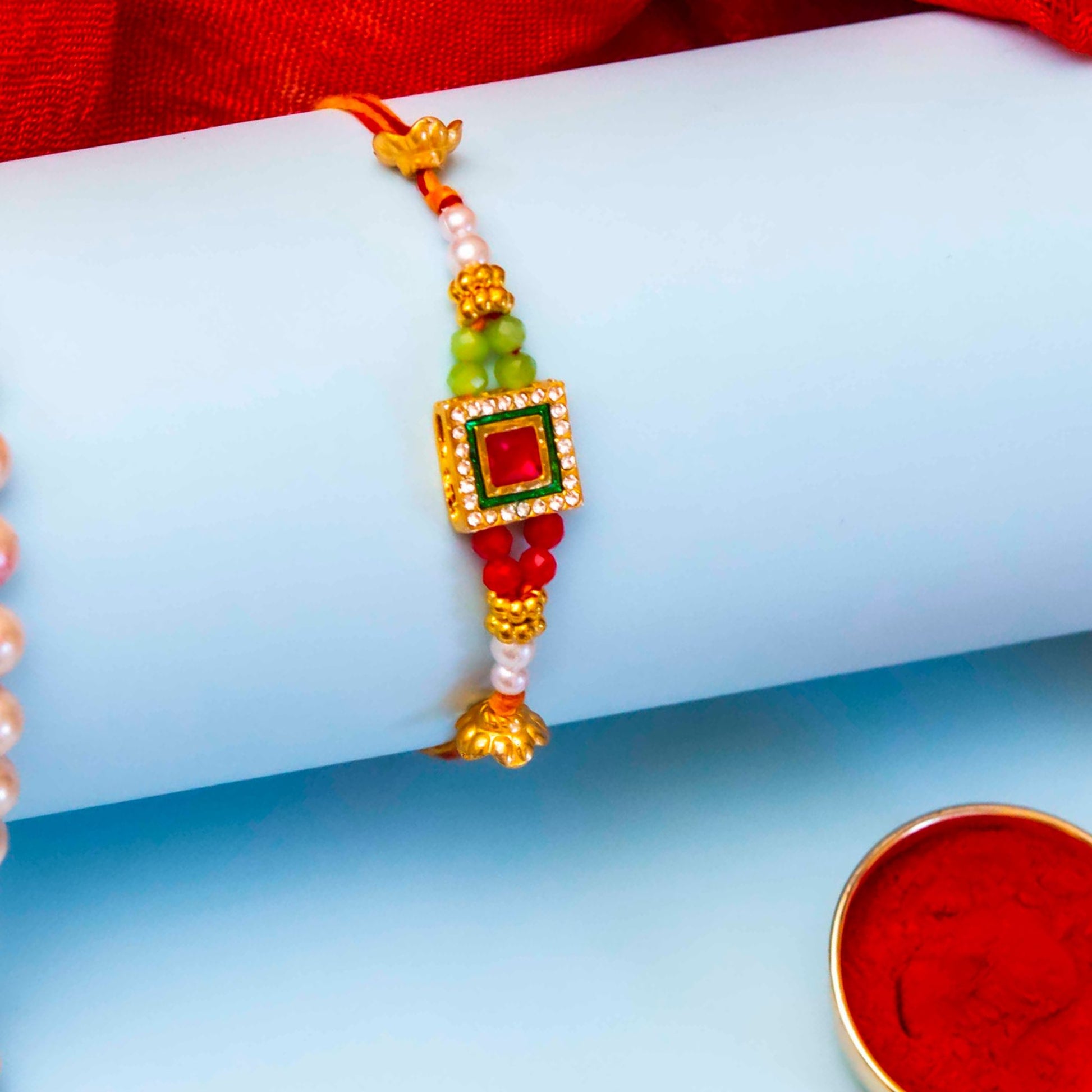Multicolor Gold, green and red stone rakhi bracelet featuring a red and green stone and beads