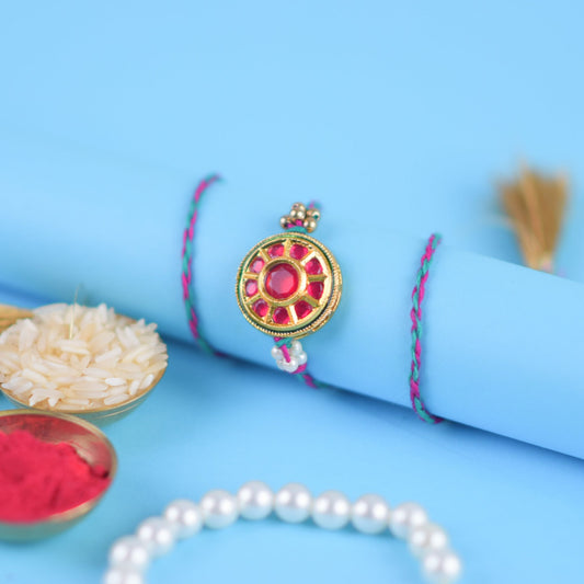 Rakhi bracelet featuring a flower, pearls, and red stone against a blue backdrop.