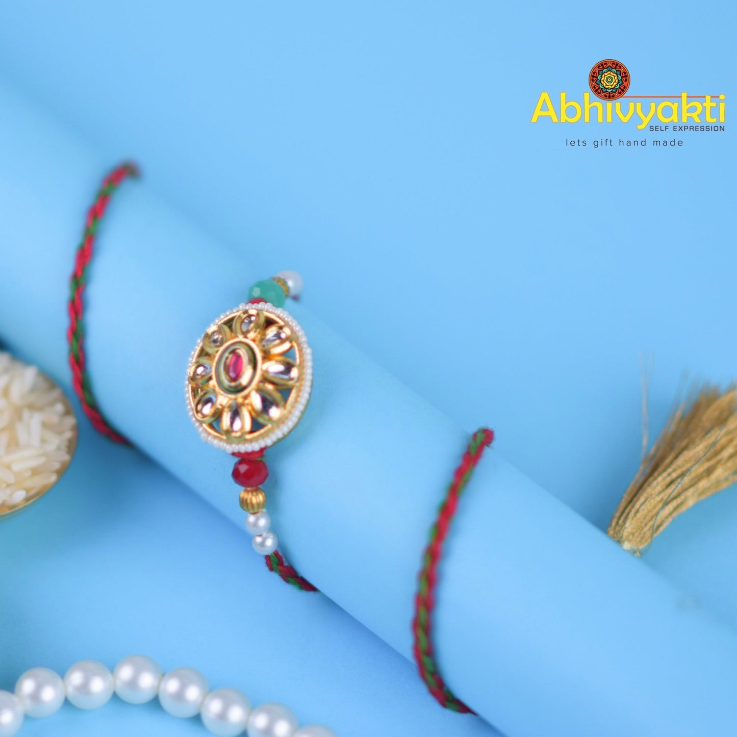 Elegant gold and red rakhi bracelet adorned with pearl, stone, and beads.