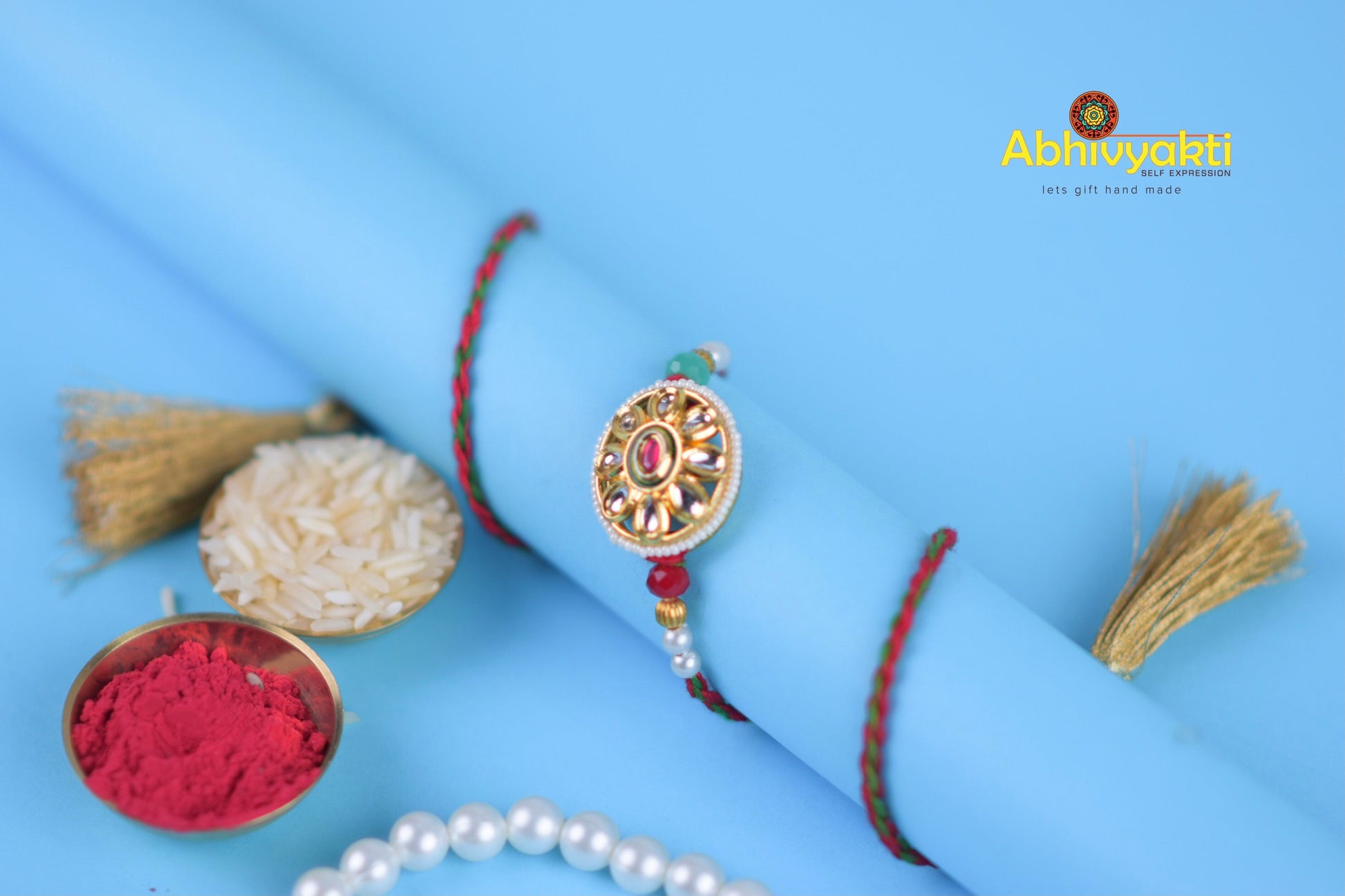 Elegant gold and red rakhi bracelet adorned with pearl, stone, and beads.