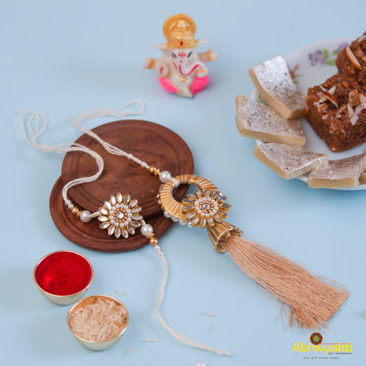 A plate holding a tassel and another plate with a cake, accompanied by a beautiful rakhi lumba adorned with stones and beads.