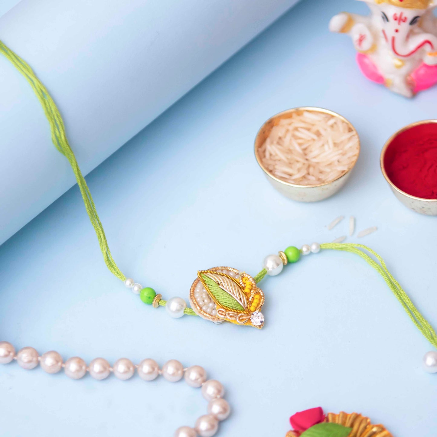 A small Zari rakhi with leaf design, beads, and stone, next to a small gift on a blue background.