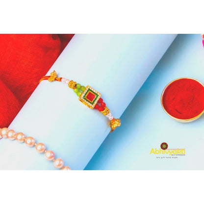 Gold and green stone rakhi bracelet featuring a red and green stone and beads.