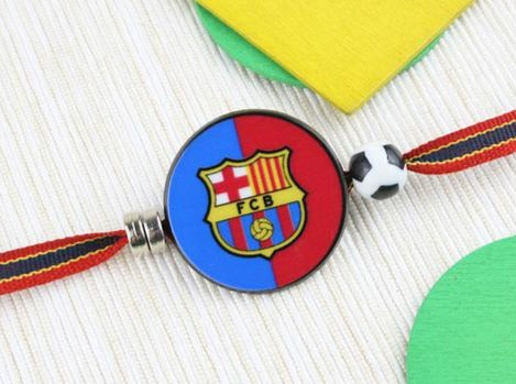 Lovely kids rakhi adorned with beads, showcasing Barcelona football badge on ribbon with soccer ball.